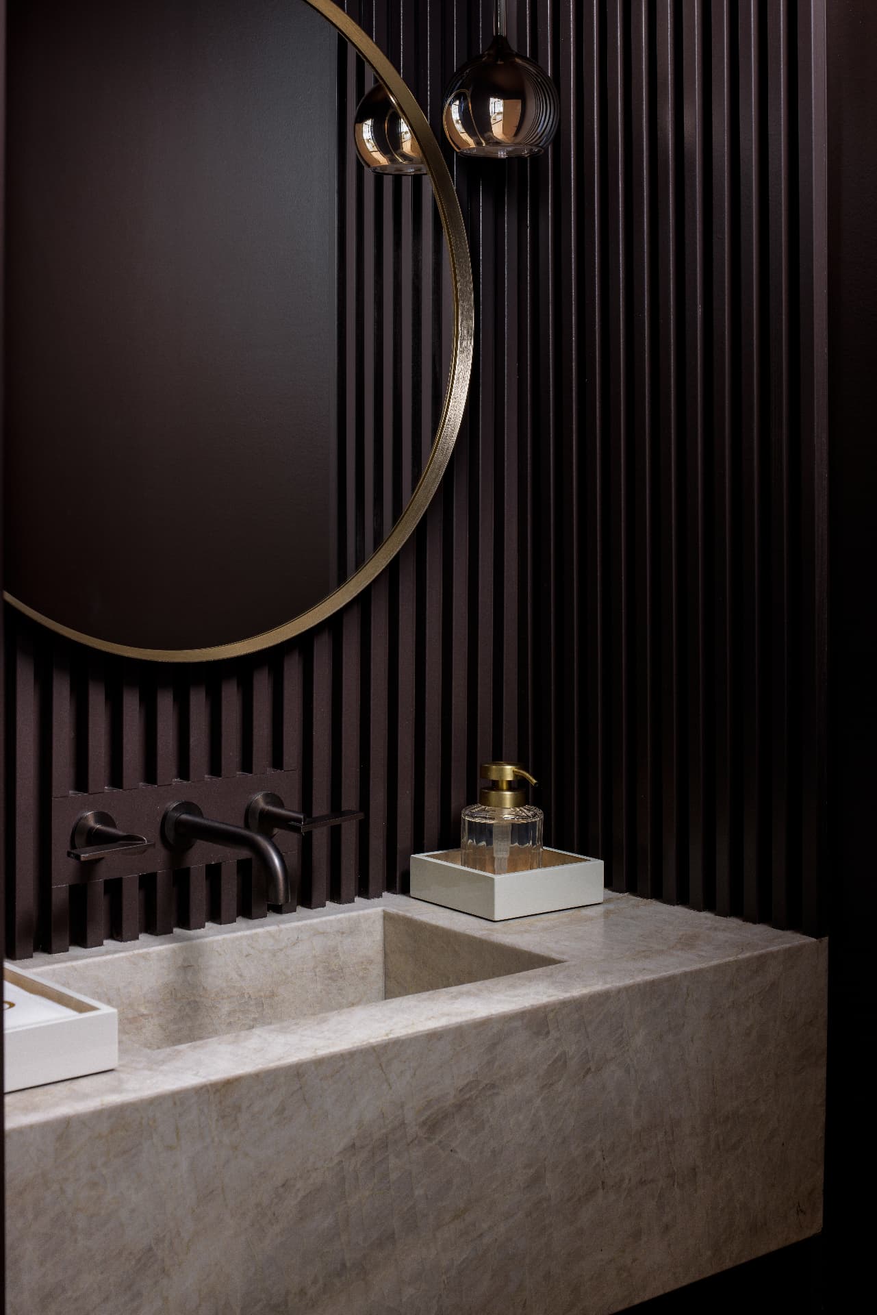 Cherry Creek powder bath with dark fluted millwork, round brass mirror, and stone vanity