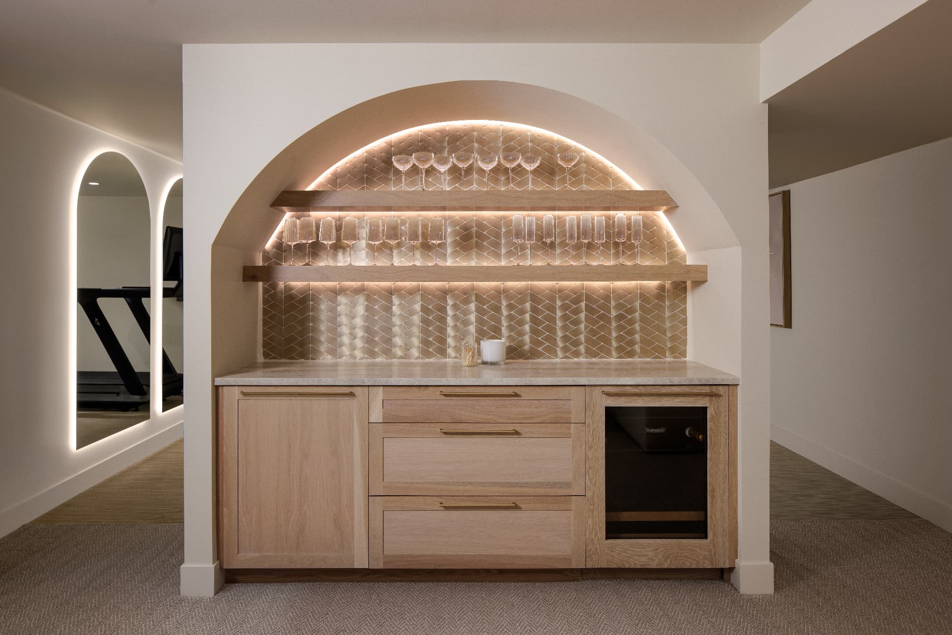 Cherry Creek lower-level bar with backlit arched alcove, oak shelving, and glassware