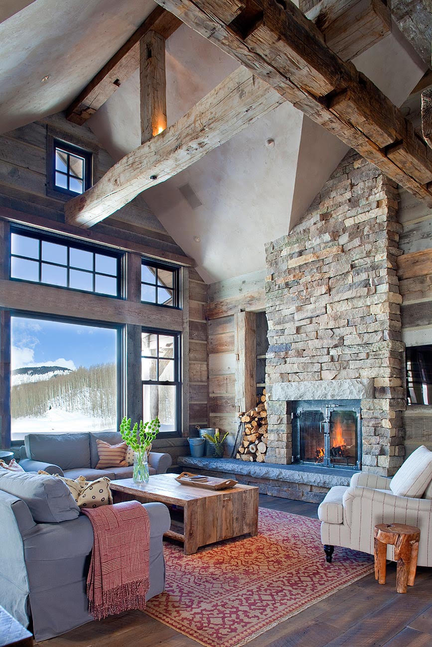 Rustic mountain living room with a stone fireplace, exposed timber beams, and a mountain view