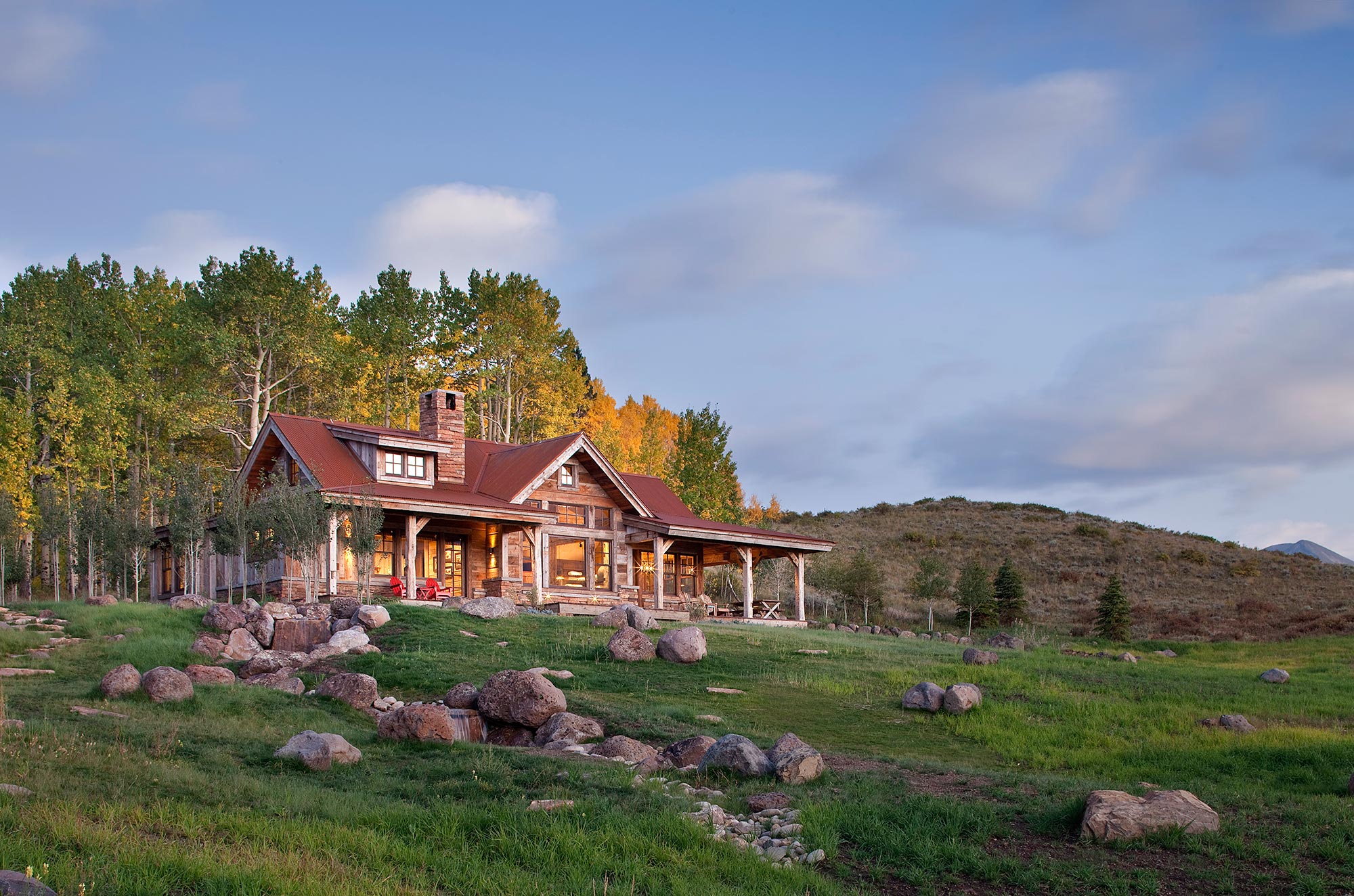 Timber-and-stone guest house on a meadow rise at golden hour