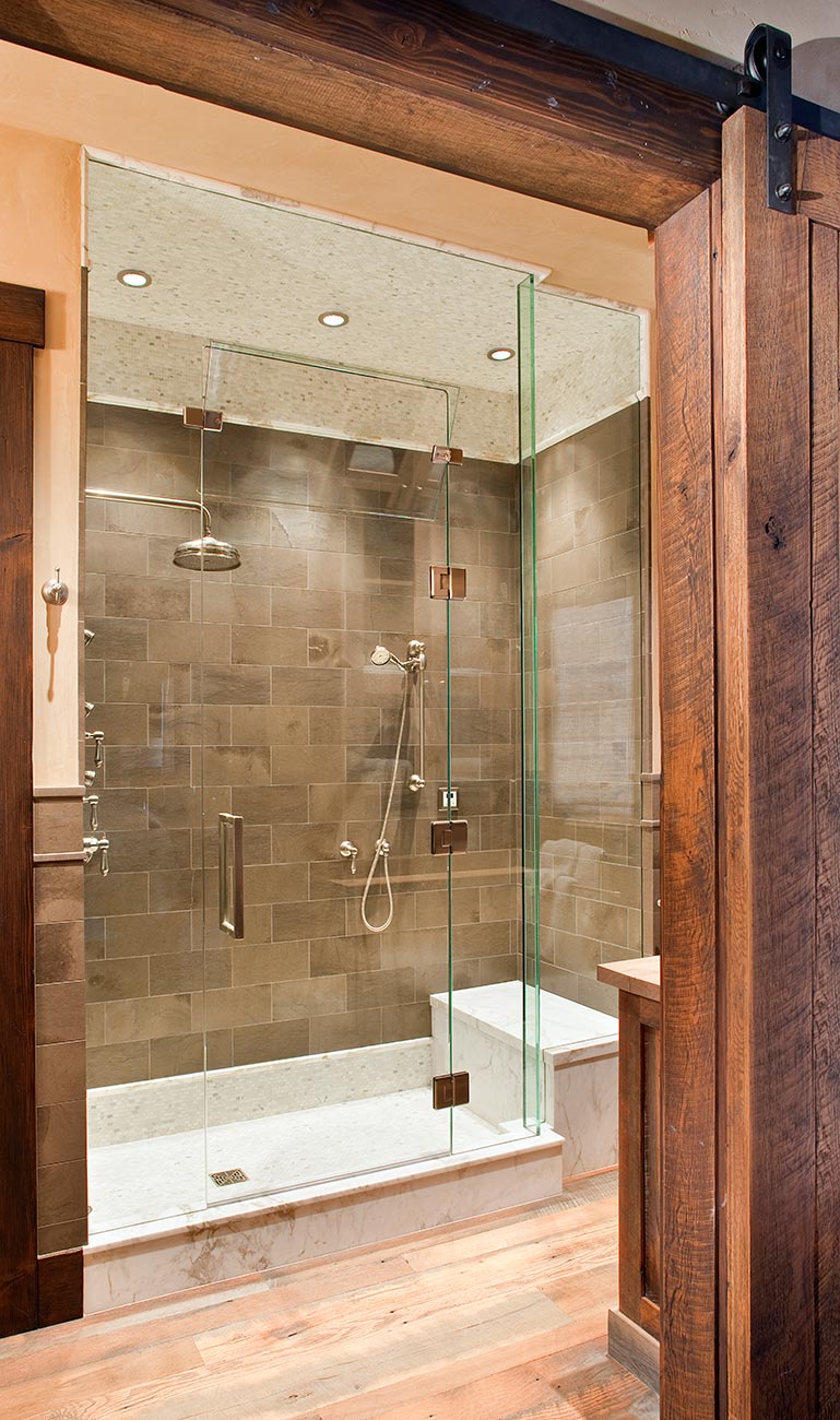 Walk-in shower with stone tile, marble bench, and a barn door
