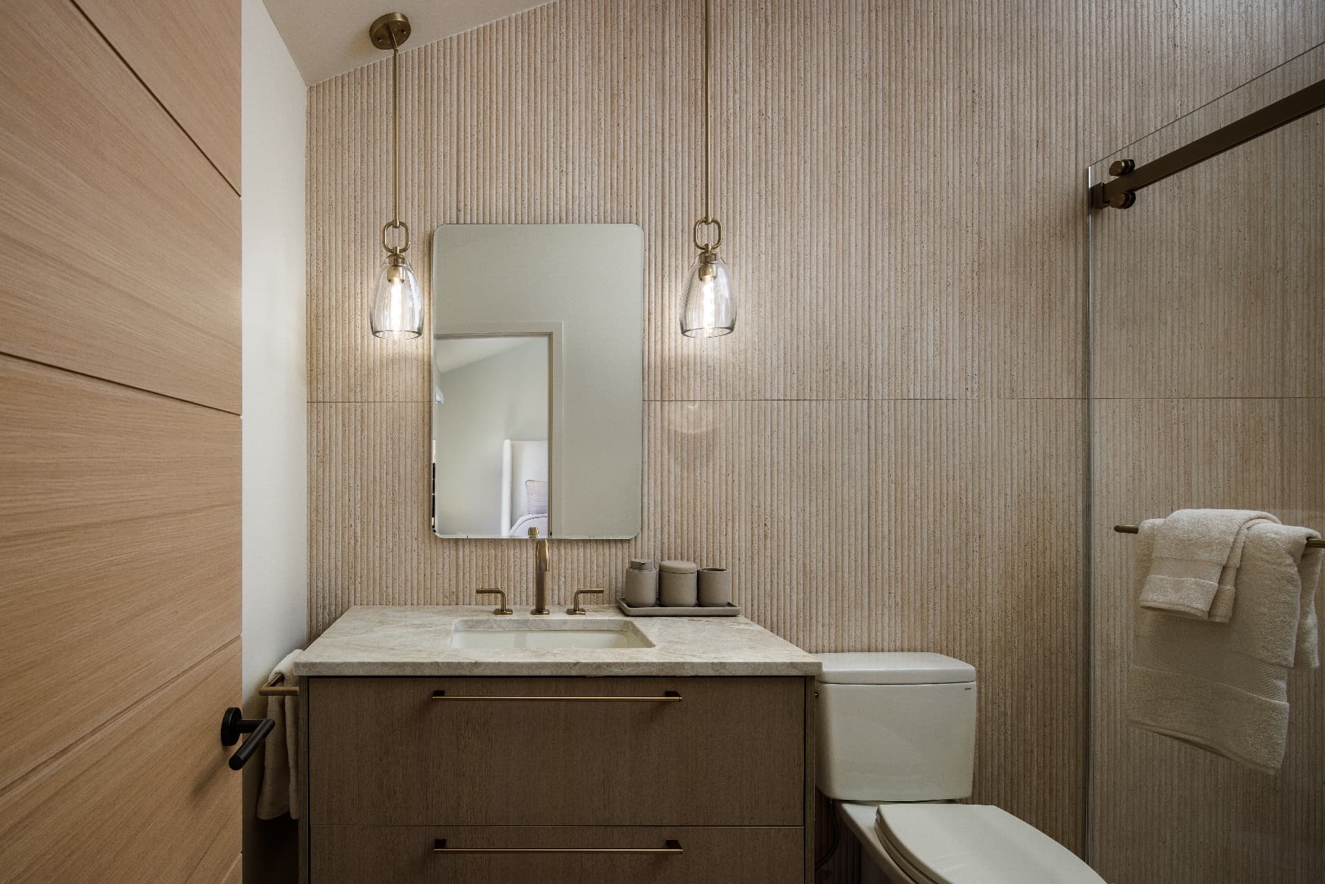 Cherry Creek guest bath with fluted travertine walls, brass pendants, and oak vanity