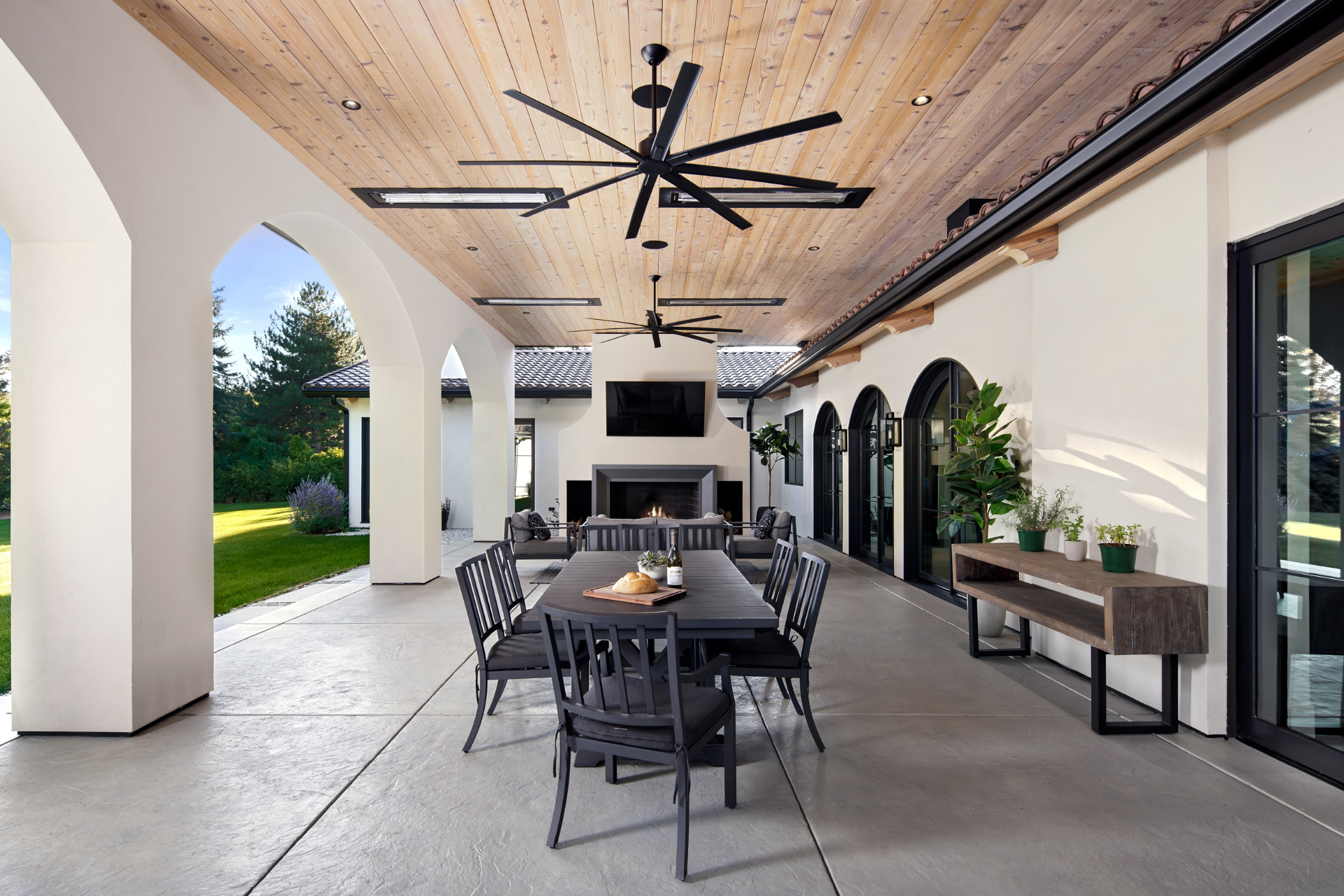 Covered outdoor loggia with cedar ceiling, fireplace, and dining table